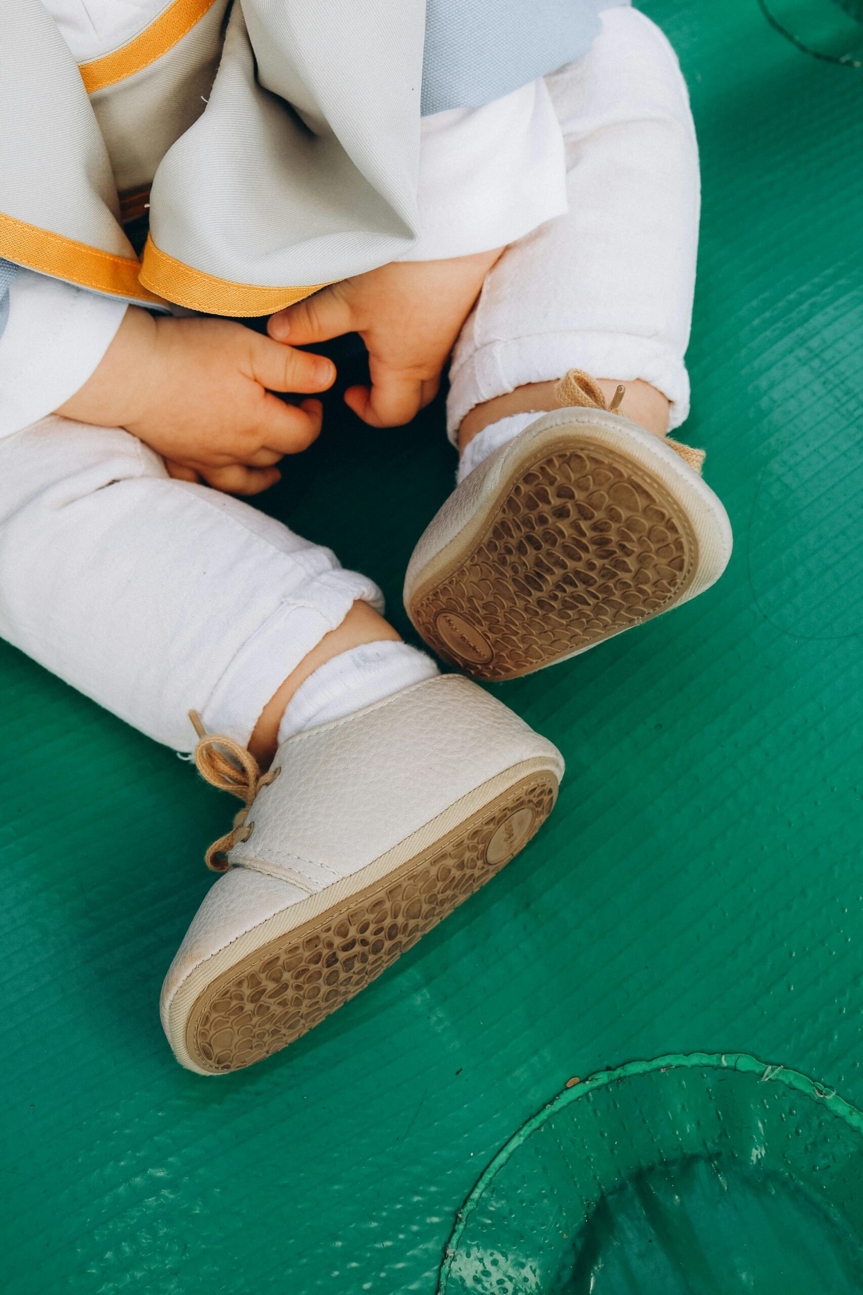 Close-up of a sitting baby wearing stylish small shoes on a green surface.