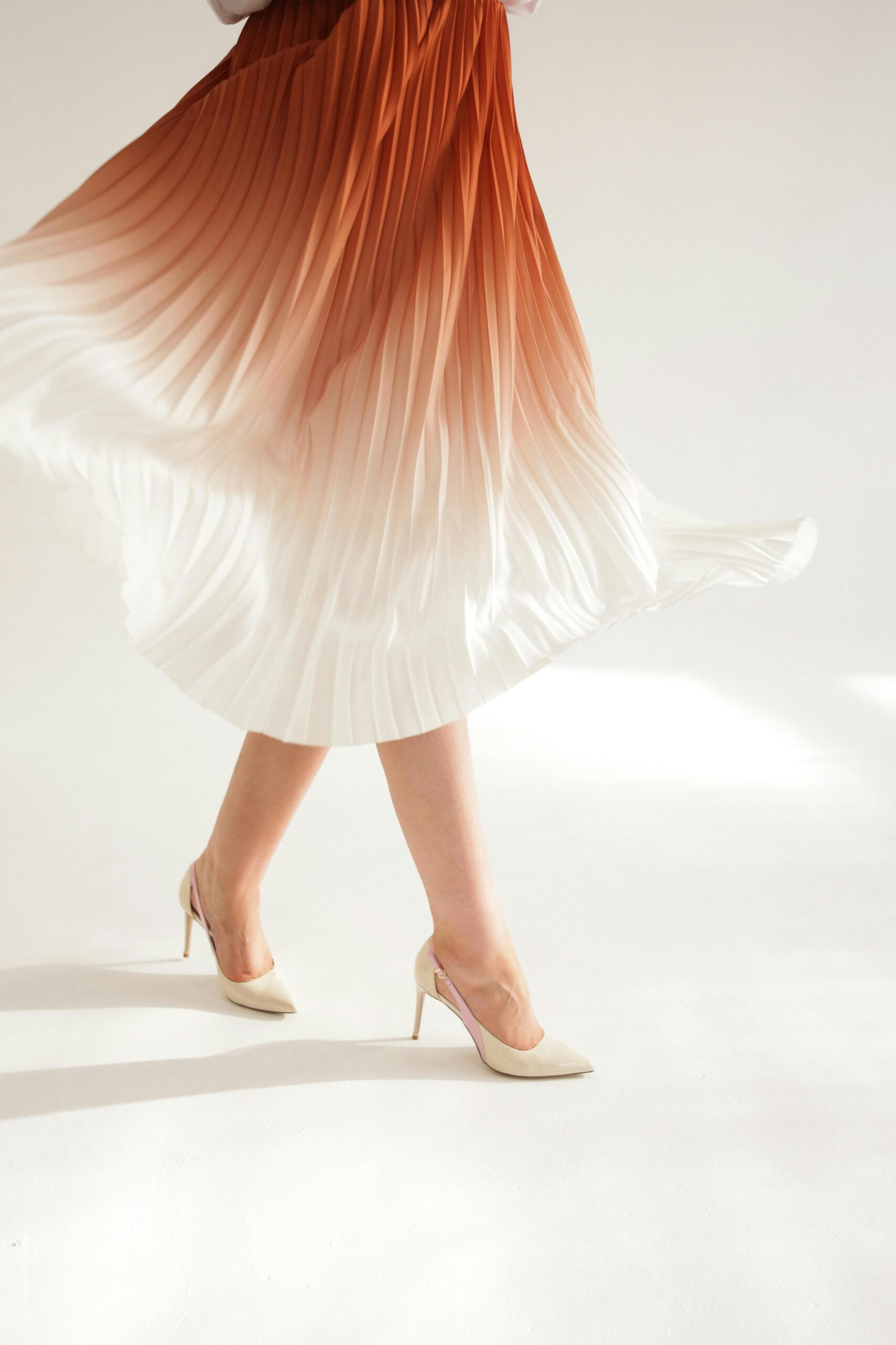 Close-up of woman twirling in an ombre pleated skirt, showcasing movement and fashion elegance.